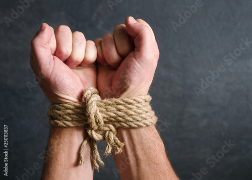 Male hands tied by a rough rope on a dark background close-up. Symbol of bondage, slavery