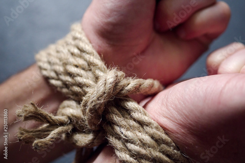Fotografie Male hands tied by a rough rope on a dark background close-up
