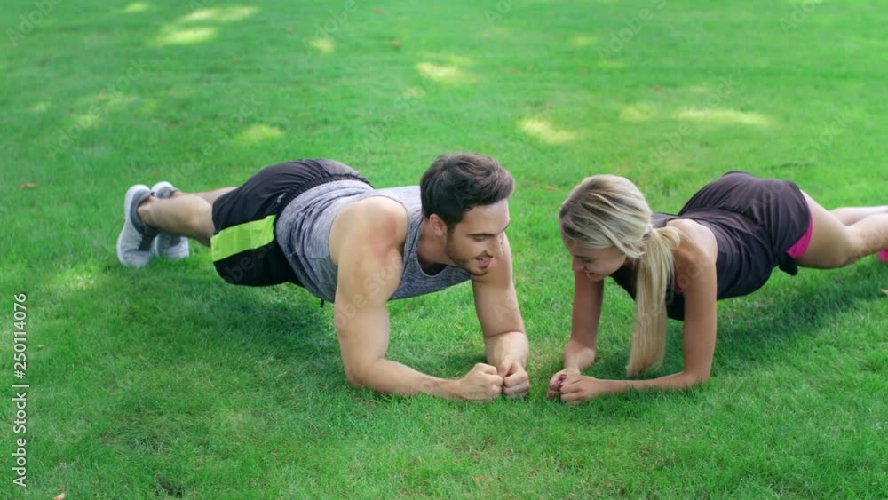 Happy man and woman standing in plank on green grass at fitness training outdoor Happy man and woman standing in plank on green grass at fitness training outdoor