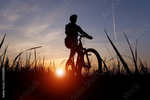 Silhouette of a cyclist against the sunset sky with sun and sunlight, copy space