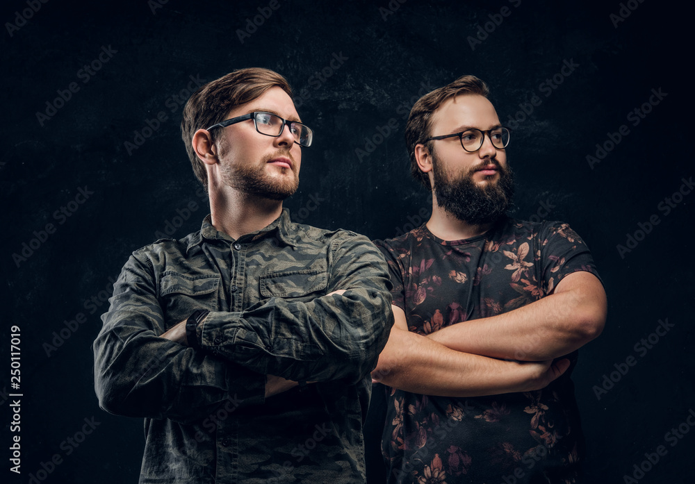 Two guys in trendy clothes posing with confident look and crossed arms. Studio photo with dark background Two guys in trendy clothes posing with confident look and crossed arms. Studio photo with dark background