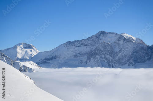 Mountain peaks covered in snow above clouds in La Plagne, French Savoy Alps. Winter scenic scenery, blue sky and stunning views. © hopsalka
