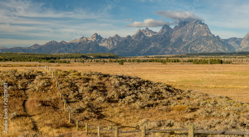 Fotografie In Wyoming the Teton mountain range with a rood fences on a farmers field