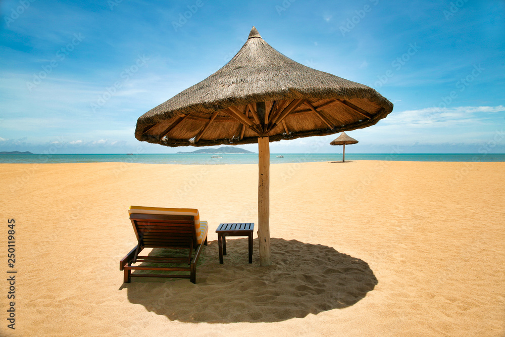 Lonely chaise longue and table, standing on a deserted beach under umbrellas of palm leaves. Sanya, Hainan