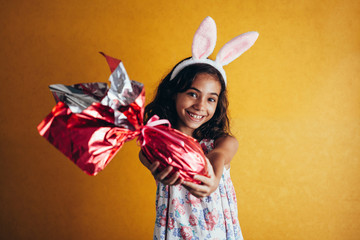 Cute little child wearing bunny ears on Easter day on color background. Girl holding chocolate easter egg