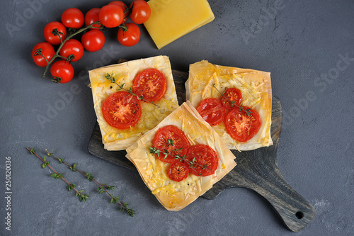 Mini pizza from puff pastry with cheese and tomatoes. The composition is complemented by cherry tomatoes and cheese. Gray background. Close-up. View from above.