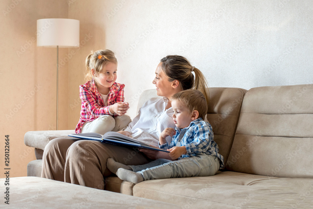 Happy mother enjoying day with children while reading book together at home