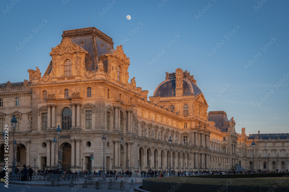 Paris, France - 02 17 2019: The roofs of the buildings of the Louvre Museum at sunset with moon