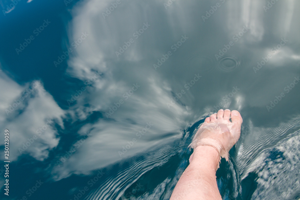 foot of a woman submerged in the crystal clear waters of a lake where the clouds are reflected