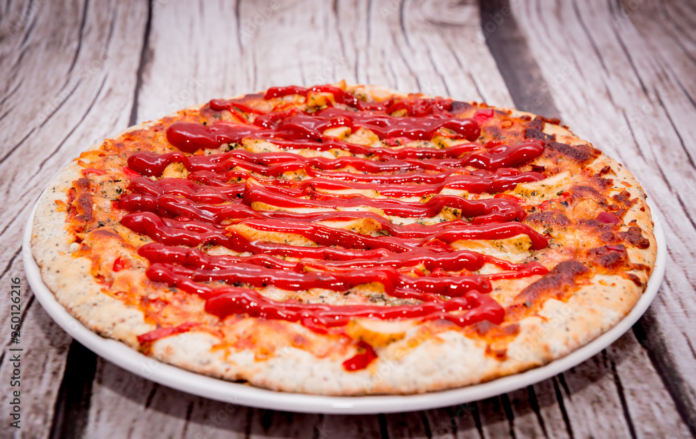 Pizza with ketchup on a wooden background. Pizza with chicken and cheese on a white background. The concept of eating pizza, preparing a quick dish for guests. Pizza with ketchup on a wooden background. Pizza with chicken and cheese on a white background. The concept of eating pizza, preparing a quick dish for guests.