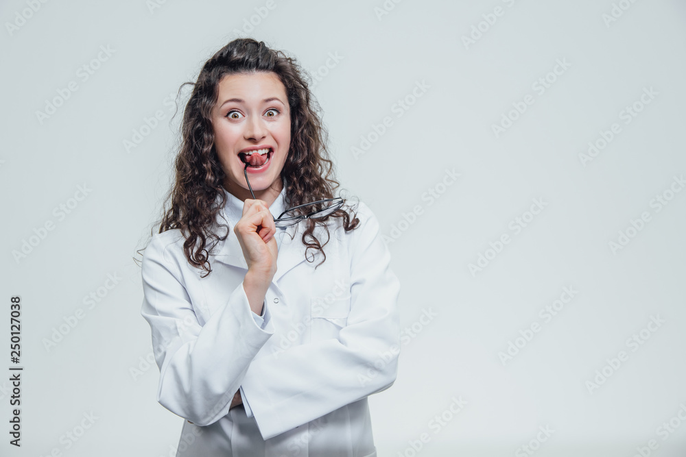 Beautiful smiling woman - the doctor looking at the camera half the turn. Happy and funny woman wearing a medical front portrait over a gray background. Medical Concepts.