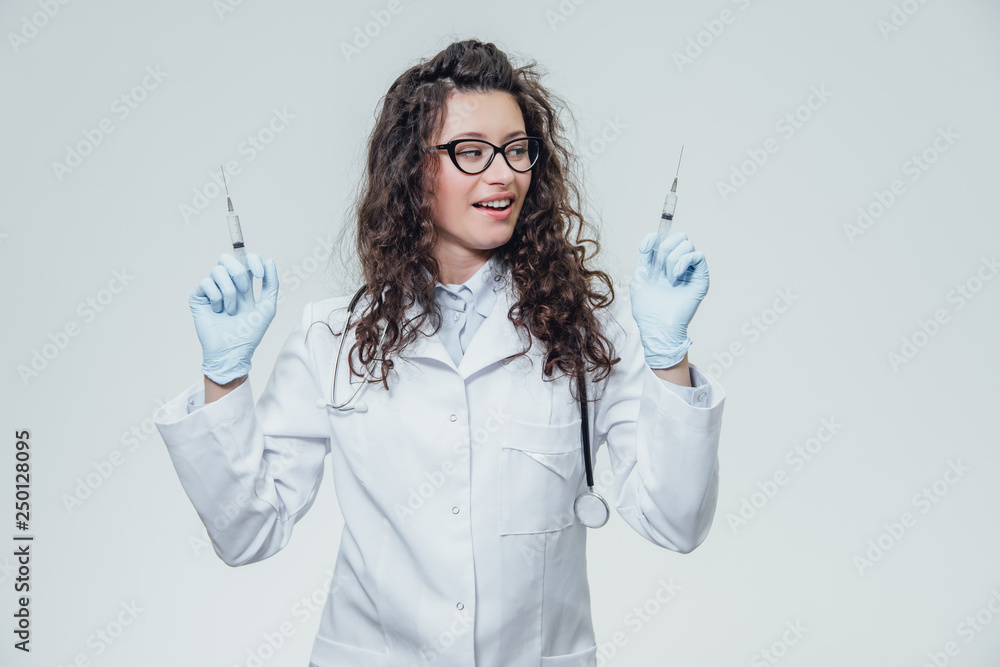 Doctor of medical staff in white uniform holding syringes in his hands on a gray background and looking directly at the camera. Health and Medical Aid, Concept. Portrait of a nurse. Doctor of medical staff in white uniform holding syringes in his hands on a gray background and looking directly at the camera. Health and Medical Aid, Concept. Portrait of a nurse.