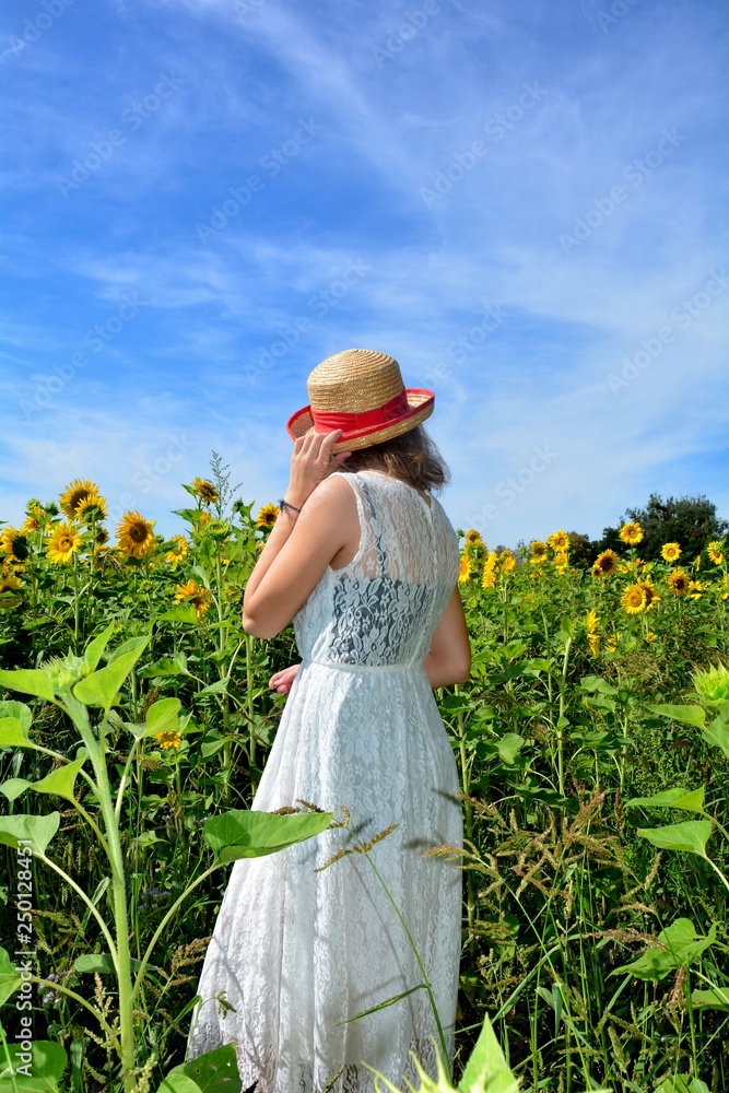 Naklejka premium Rücken eines Mädchen mit Strohhut im Sonnenblumen Feld mit blauem Himmel