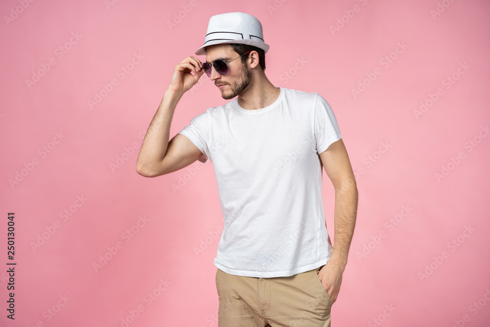 Cheerful young man in hat and sunglasses standing and smiling over pink background. Cheerful young man in hat and sunglasses standing and smiling over pink background.