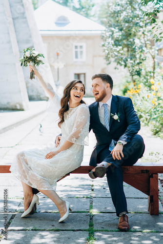 Stylish and beautiful wedding couple sitting on the bench and having fun