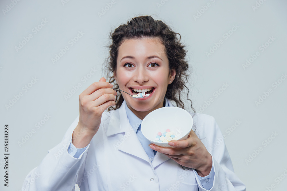 The girl doctor in a white dressing gown is on a gray background. Girl's Dependence on Drugs. He wants to eat medicine from a plate. The girl doctor in a white dressing gown is on a gray background. Girl's Dependence on Drugs. He wants to eat medicine from a plate.