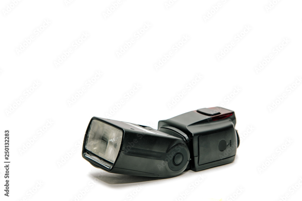View of a black flash lamp isolated on a white background. The concept of triggering a flash for the camera. Adequate lighting during photography. View of a black flash lamp isolated on a white background. The concept of triggering a flash for the camera. Adequate lighting during photography.