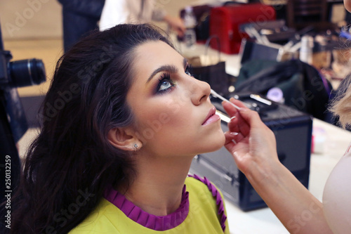 make-up artist makes a professional make-up model with blue eyes and dark hair