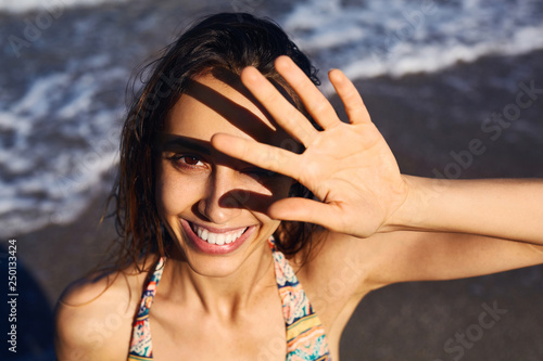 Portrait of a young smiling woman at the beach. a woman closes the face from the Sun by the hand