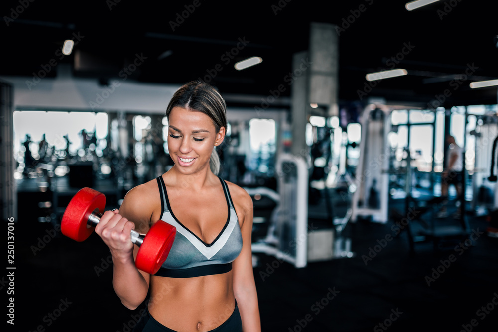 Fototapeta premium Positive young woman in sportswear working out with dumbbell.