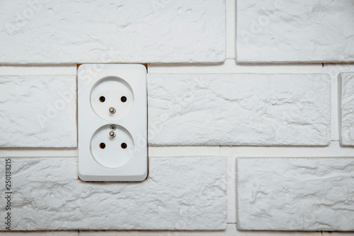 White electric socket on a white, bright brick. The concept of electric power consumption, the use of electricity. Savings on energy supply, power supply of various household items. photo