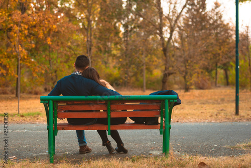 Young sweet couple embrace on a bench in park watching a beautiful sunset, enjoying their love and nature.