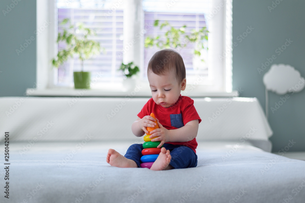 Baby boy with coloured pyramid toy on bed in his room Baby boy with coloured pyramid toy on bed in his room