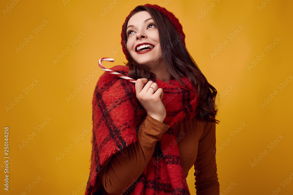 Beautiful brunette woman in red hat with big knitted scarf holding a candy Beautiful brunette woman in red hat with big knitted scarf holding a candy