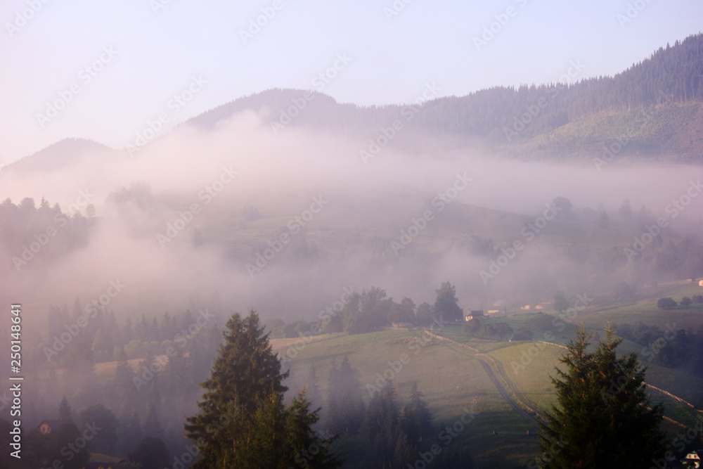 Beautiful landscape of mountains with light fog. Mountain village in the fog at early morning. Carpathian mountains view.