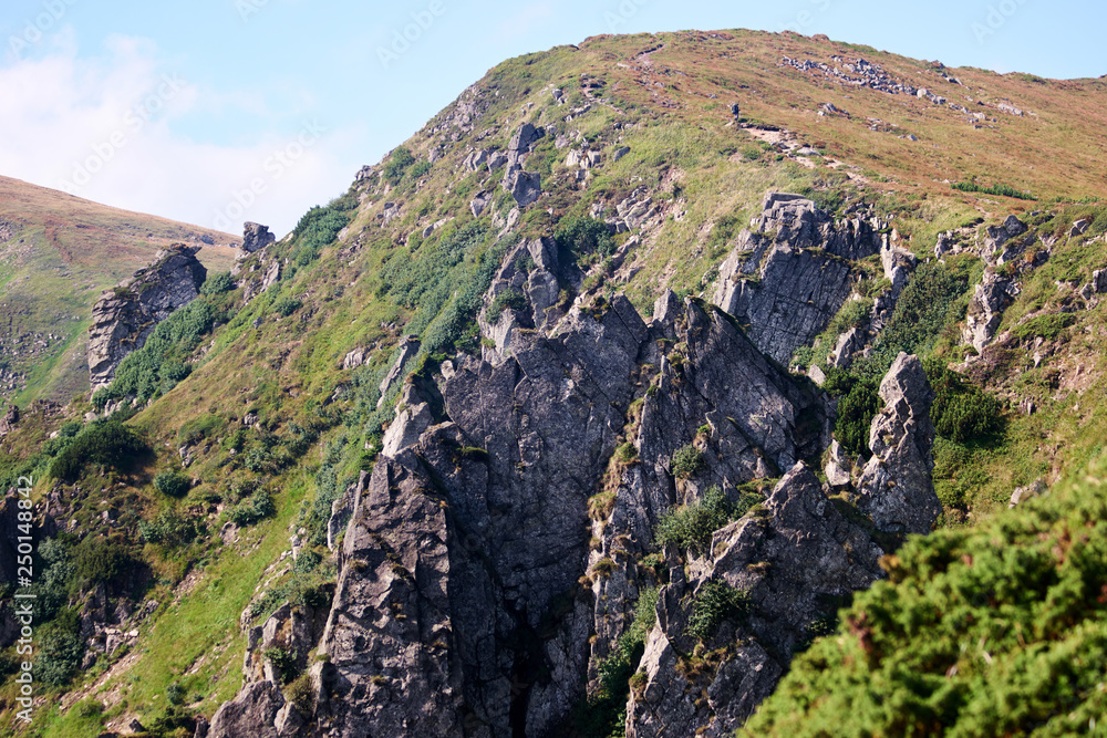 Rocky cliffs on mountain slope. Rocky grassy mountain cliff under blue sky. Trail to mount Hoverla. Beautiful sunny day. Rocky cliffs on mountain slope. Rocky grassy mountain cliff under blue sky. Trail to mount Hoverla. Beautiful sunny day.