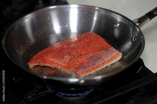 Wild caught Coho salmon frying in a pan with the skin side down.