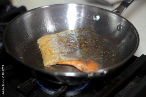 Wild caught Coho salmon frying in a pan with the skin side up.