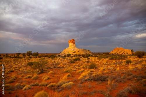 Chambers Pillar, Northern Territory; desert monument with clouds, red sand and horizon photo