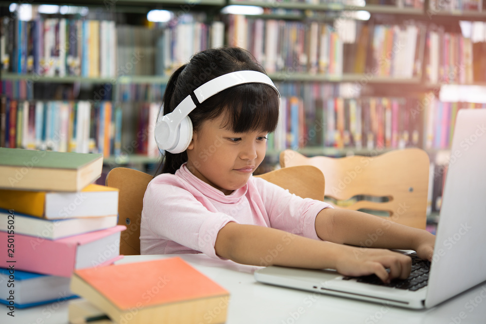 Cute asian little girl reading a book and headphones listening to music,