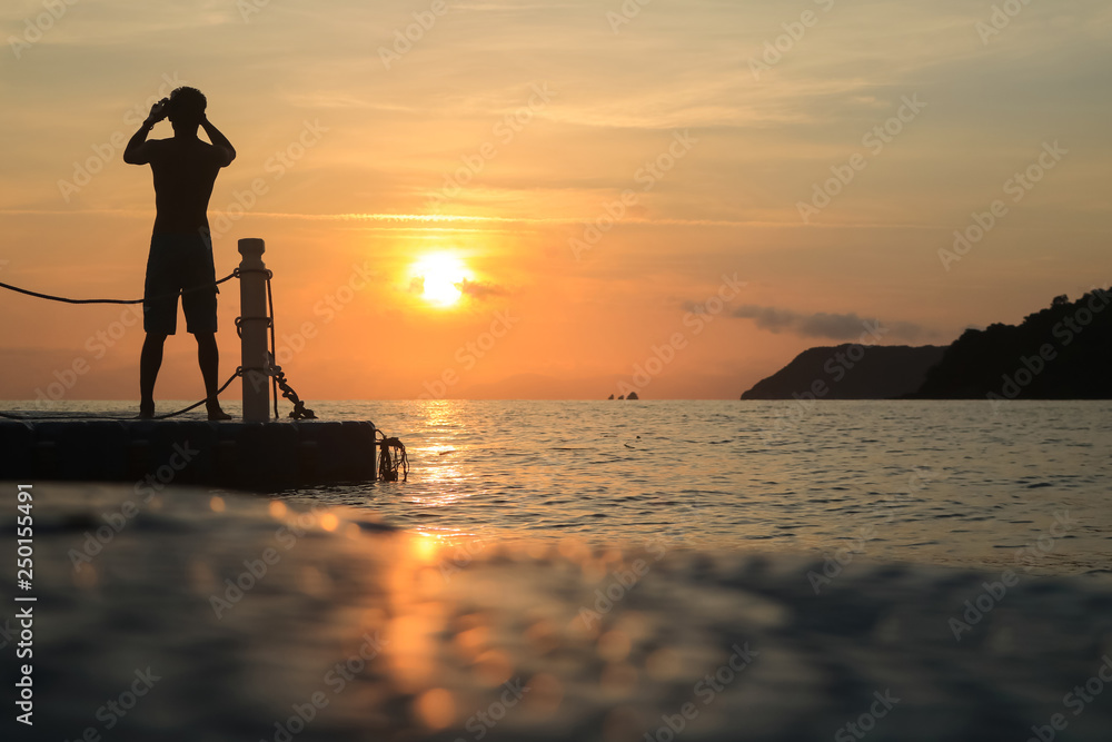 Asian man standing and jumping on floating pier at sunrise , Silhouette body of asian people early morning on the beach