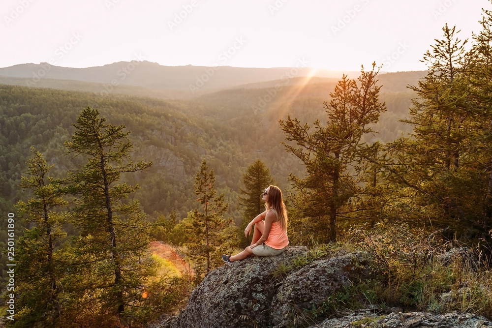blonde woman tourist sitting on a rock in the mountains under the sunset in the summer blonde woman tourist sitting on a rock in the mountains under the sunset in the summer
