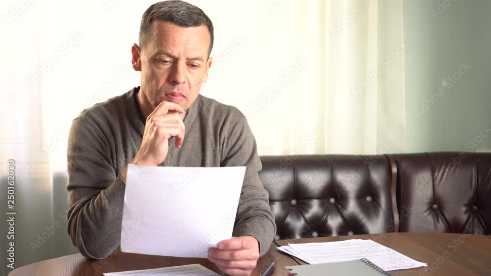 Unhappy sad man reading letter, bill, bank statement paper or tax document Unhappy sad man reading letter, bill, bank statement paper or tax document