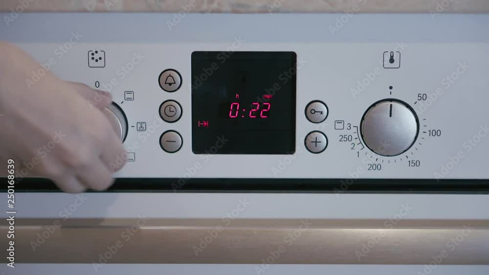 Female hand includes Metallic Toggle Switch of the Cooker Oven. Close-up View. Digital Clock of oven. Front panel of modern metalic oven, red indicators, new shiny buttons. Modern design in details. Female hand includes Metallic Toggle Switch of the Cooker Oven. Close-up View. Digital Clock of oven. Front panel of modern metalic oven, red indicators, new shiny buttons. Modern design in details.