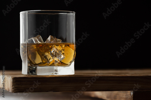 Glass of whiskey with ice cubes on a wooden table and dark background.