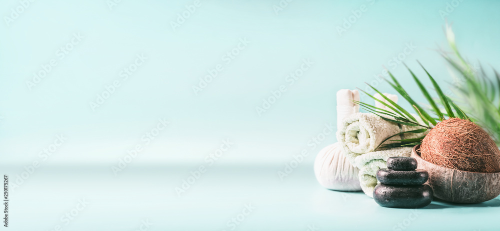 Tropical spa setting background with coconut, palm leaves at light blue.  Massage treatment. Rolled towels, compress balls and hot stone. Beauty,  wellness and body care. Banner or template. Copy space Stock Photo |