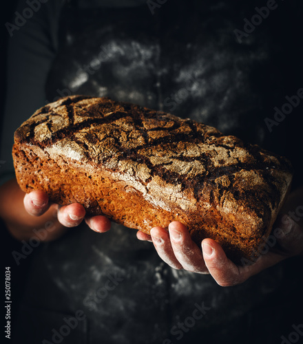 Female hands hold dark rye bread. Baker with fresh bread on a dark background.