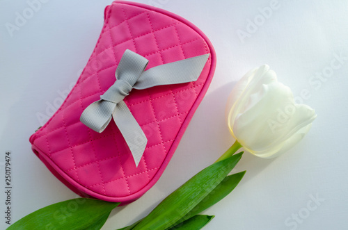white tulip flower. pink cosmetic bag, makeup brushes, cosmetics on white background
