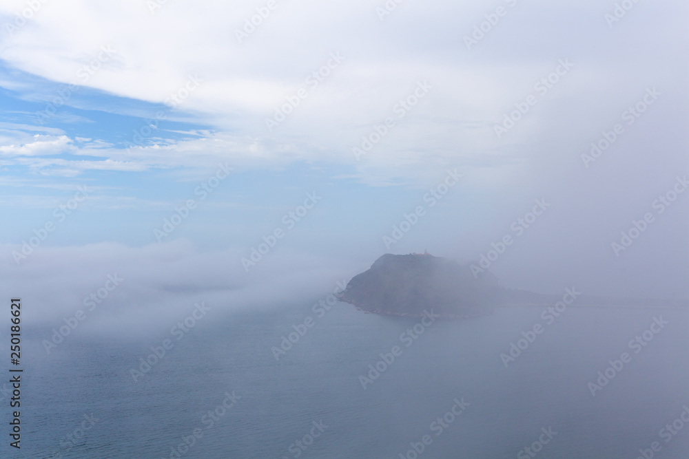 Low clouds and mist over ocean concealing a small island - mystical landscape Low clouds and mist over ocean concealing a small island - mystical landscape