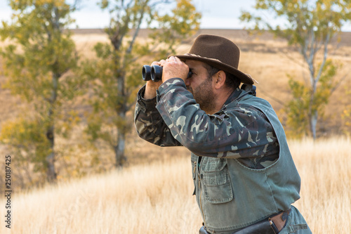 A hunter in a hat with binoculars looks out for prey	