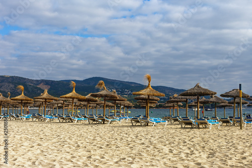 sun beds and umbrellas on a sandy beach against a blue sea and a cloudy sky