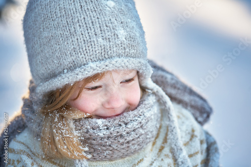 Little cheerful girl in a snow-covered hat, scarf and sweater. Snow around