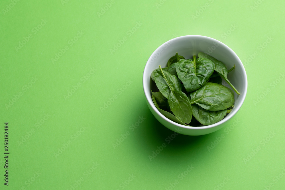 Babe spinach leaves in white bowl isolated on green background Babe spinach leaves in white bowl isolated on green background