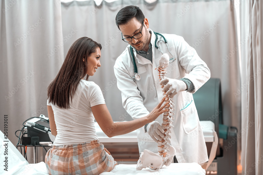 Female patient sitting with backs turned showing on spine model where ...