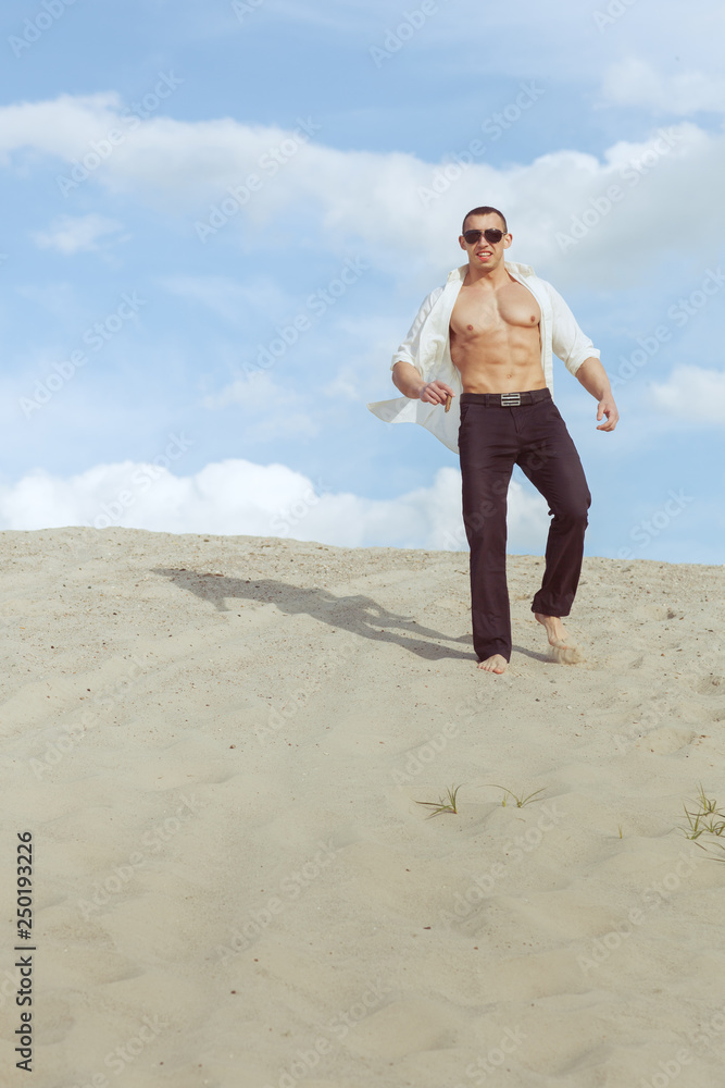 Young macho man with glasses and a cigar in his hand walking through the desert. Young macho man with glasses and a cigar in his hand walking through the desert.