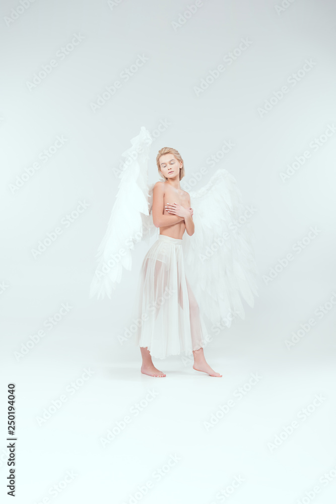 beautiful woman with angel wings covering breasts and posing with eyes closed isolated on white beautiful woman with angel wings covering breasts and posing with eyes closed isolated on white